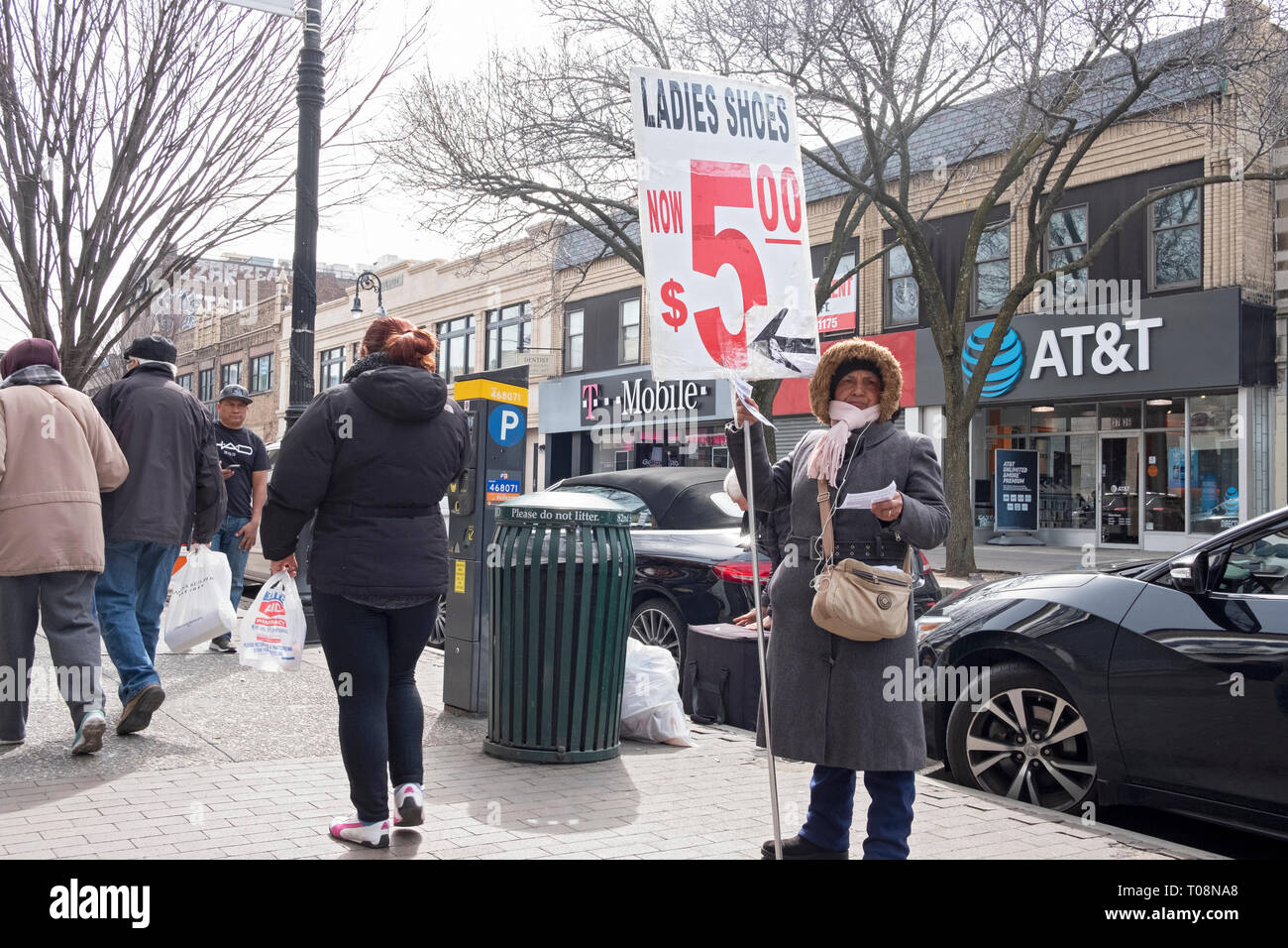 Frau mit einem großen Schild versucht, Käufer zu einer kostengünstigen Schuhgeschäft auf 82nd St. in Jackson Heights, Queens, New York City in der Nähe des #7 Zug zu gewinnen. Stockfoto