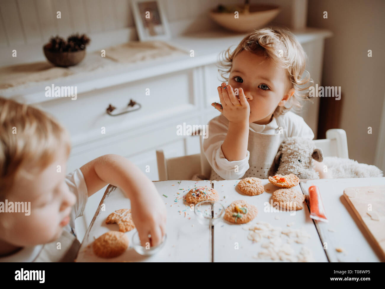 Zwei kleine kleinkind Kinder am Tisch sitzen, Dekorieren und essen Kuchen zu Hause. Stockfoto
