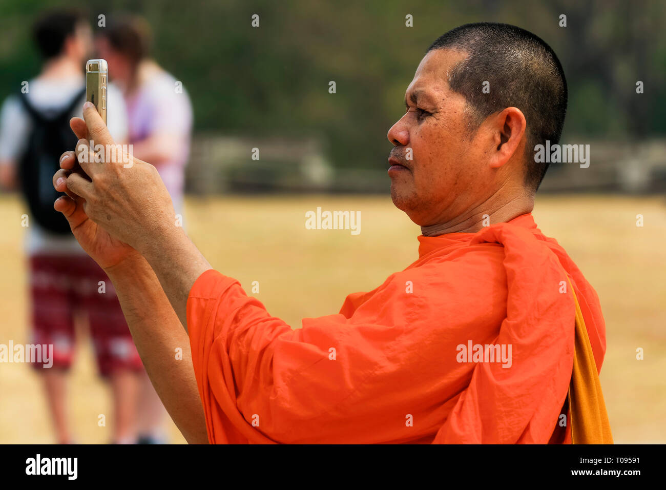Buddhst Mönch im orangen Gewand nimmt Fotos auf Handy an der buddhistischen Tempelanlage Angkor Wat, Angkor, Siem Reap, Kambodscha. Stockfoto