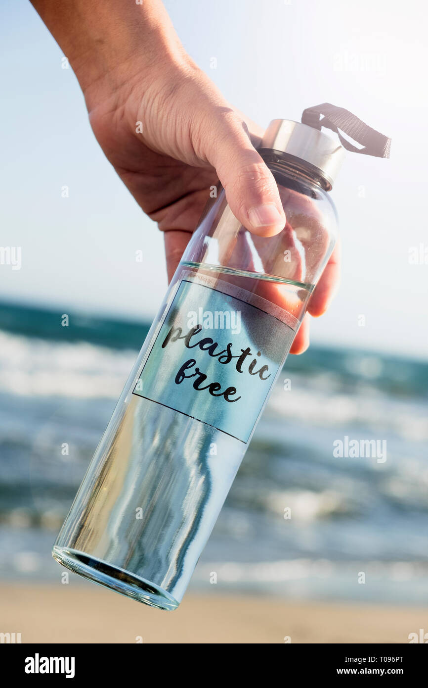 Nahaufnahme von einem kaukasischen Mann hält ein Glas wiederverwendbare Trinkflasche mit dem Text aus Kunststoff in Es geschrieben, am Strand, mit dem Meer in der backgro Stockfoto