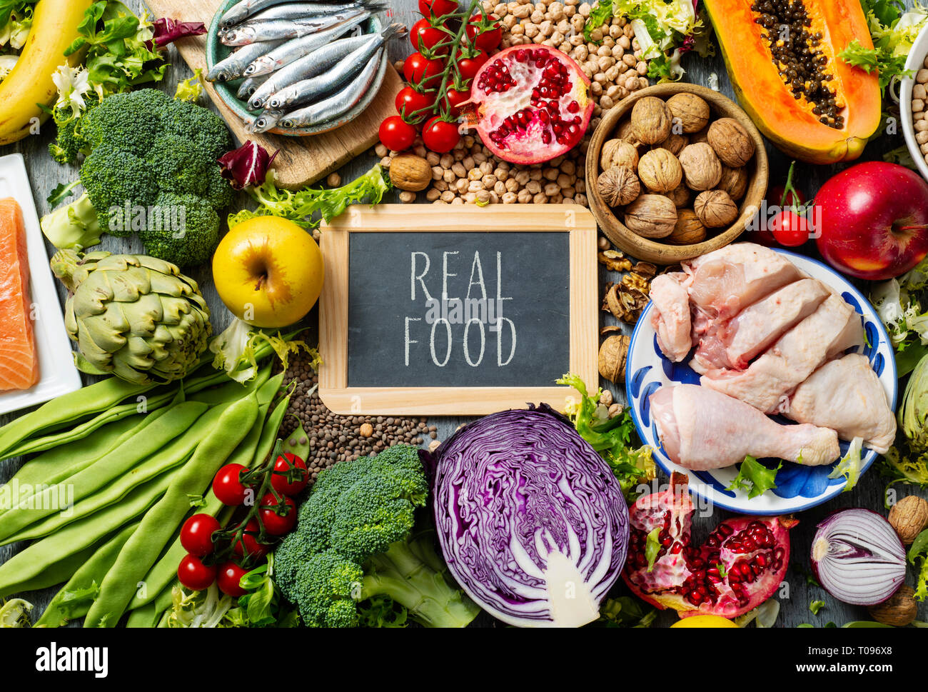Eine Tafel mit dem Text Real Food geschrieben, auf einem Haufen unverarbeitete Nahrungsmittel, wie z. B. verschiedene rohe Früchte und Gemüse, Hülsenfrüchte und Nüsse, Stockfoto