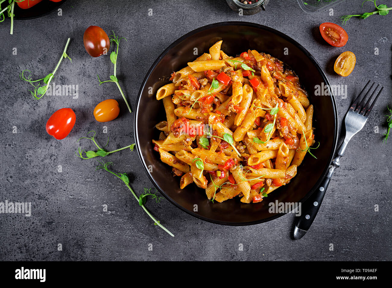Penne Pasta in Tomatensauce mit Fleisch, Tomaten mit Erbse Sprößlinge auf einen dunklen Tisch eingerichtet. Ansicht von oben Stockfoto