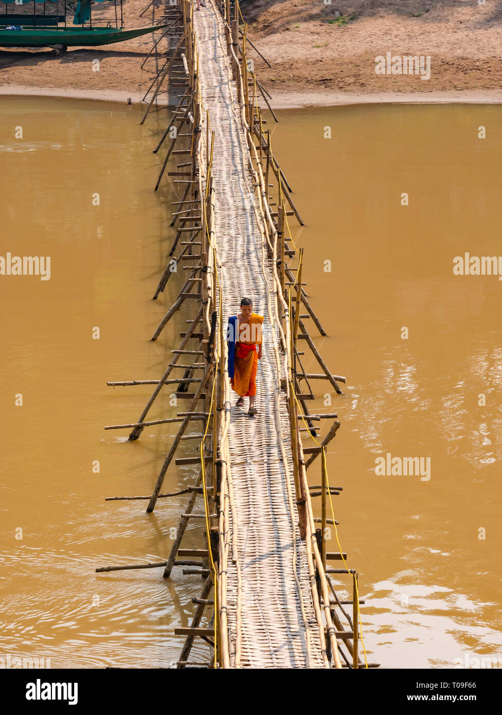 Buddhistischer Mönch im orangen Gewand gehen über Bambus Zuckerrohr Brücke über den Fluss Nam Kahn Nebenarm des Mekong, Luang Prabang, Laos, Indochina, Se Asien Stockfoto