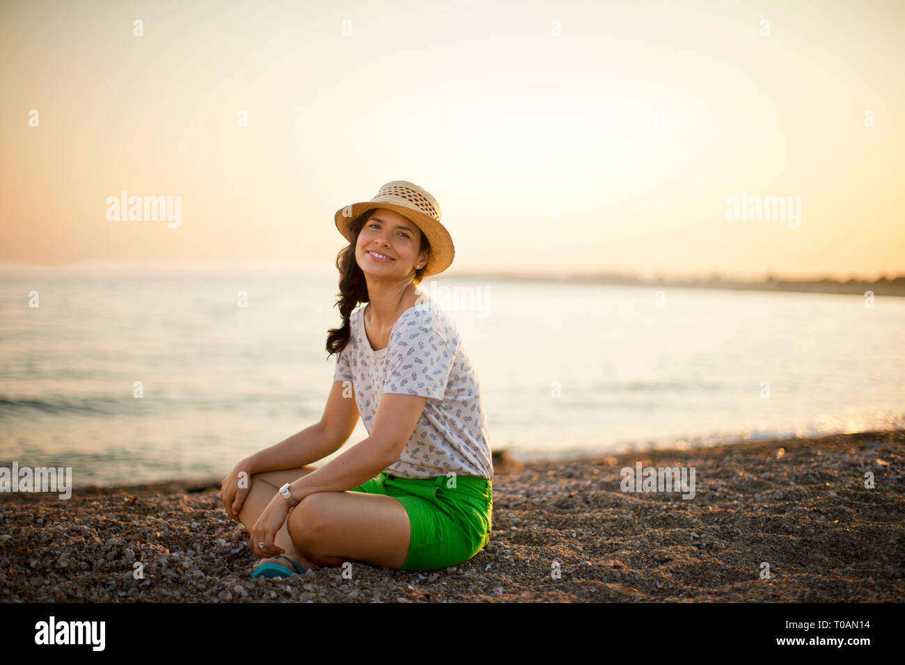 Portrait einer jungen Frau sitzt im Schneidersitz am Strand bei Sonnenuntergang. Stockfoto