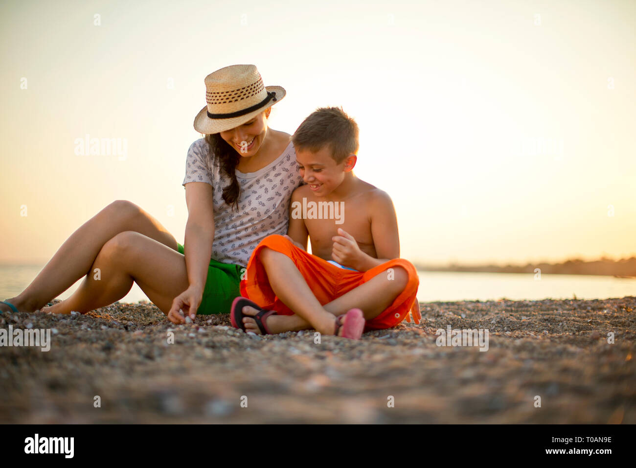 Junge und seine Mutter sitzen am Strand bei Sonnenuntergang. Stockfoto