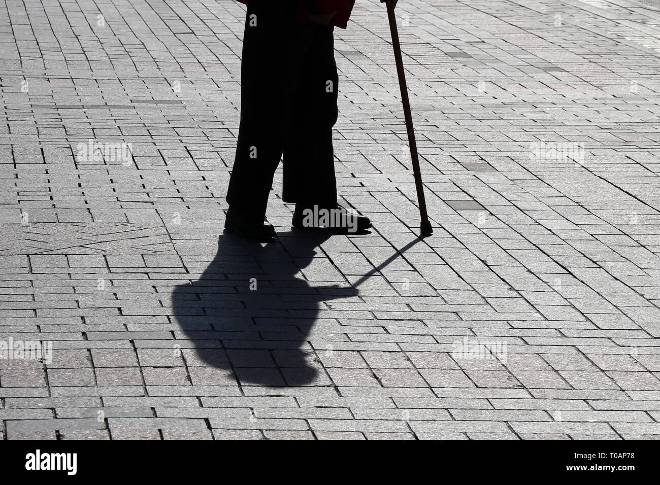 Silhouette der Altstadt von Person zu Fuß mit einem Stock, lange Schatten auf Pflaster. Konzept für Erwerbsunfähigkeit, Alter, hinkt oder blind, Erkrankungen der Wirbelsäule Stockfoto