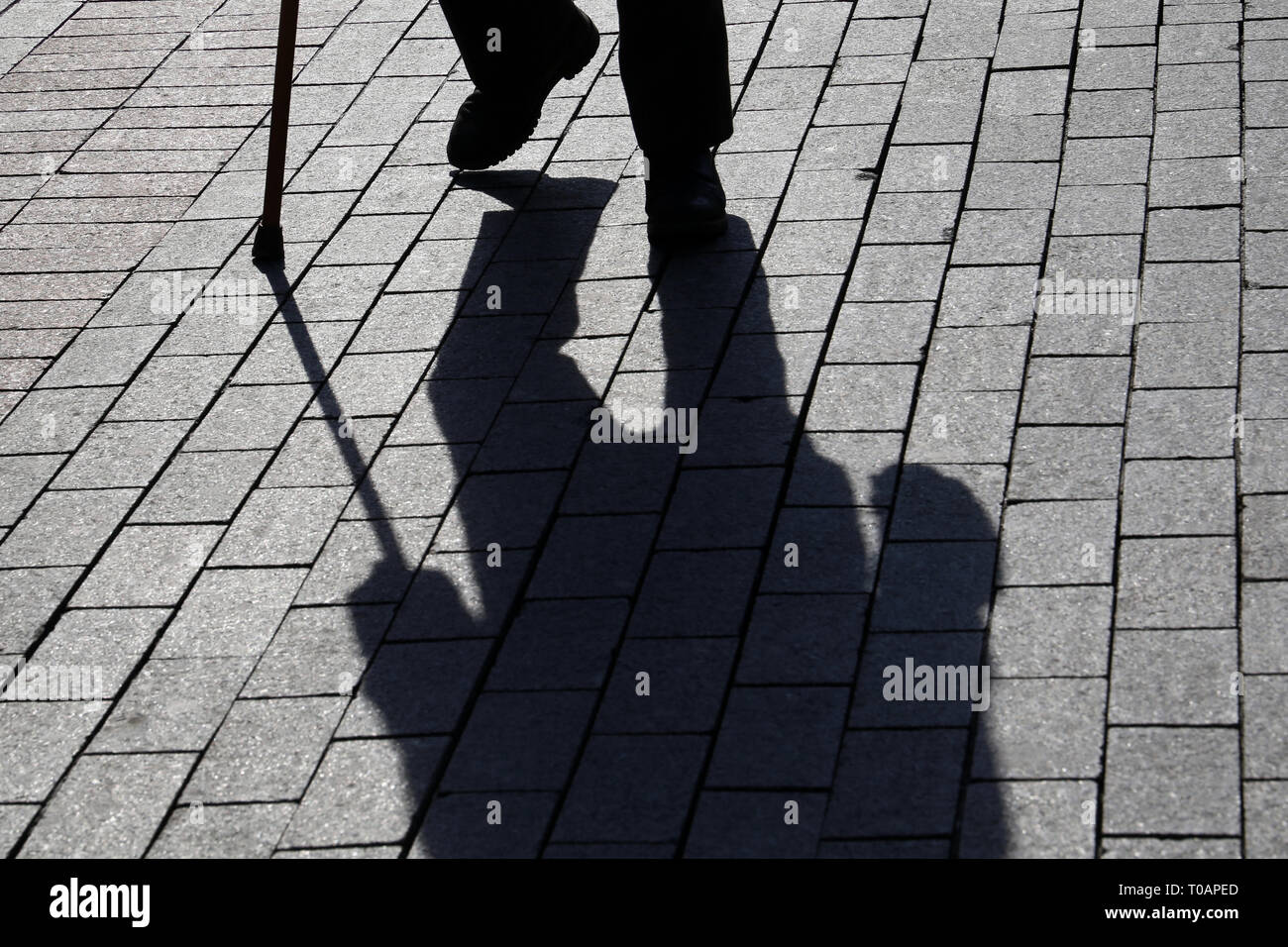 Silhouette der Mann mit einem Stock, lange Schatten auf Pflaster. Konzept der hinkt oder blind Person, Invalidität, Alter, Armut, Krankheiten der Wirbelsäule Stockfoto