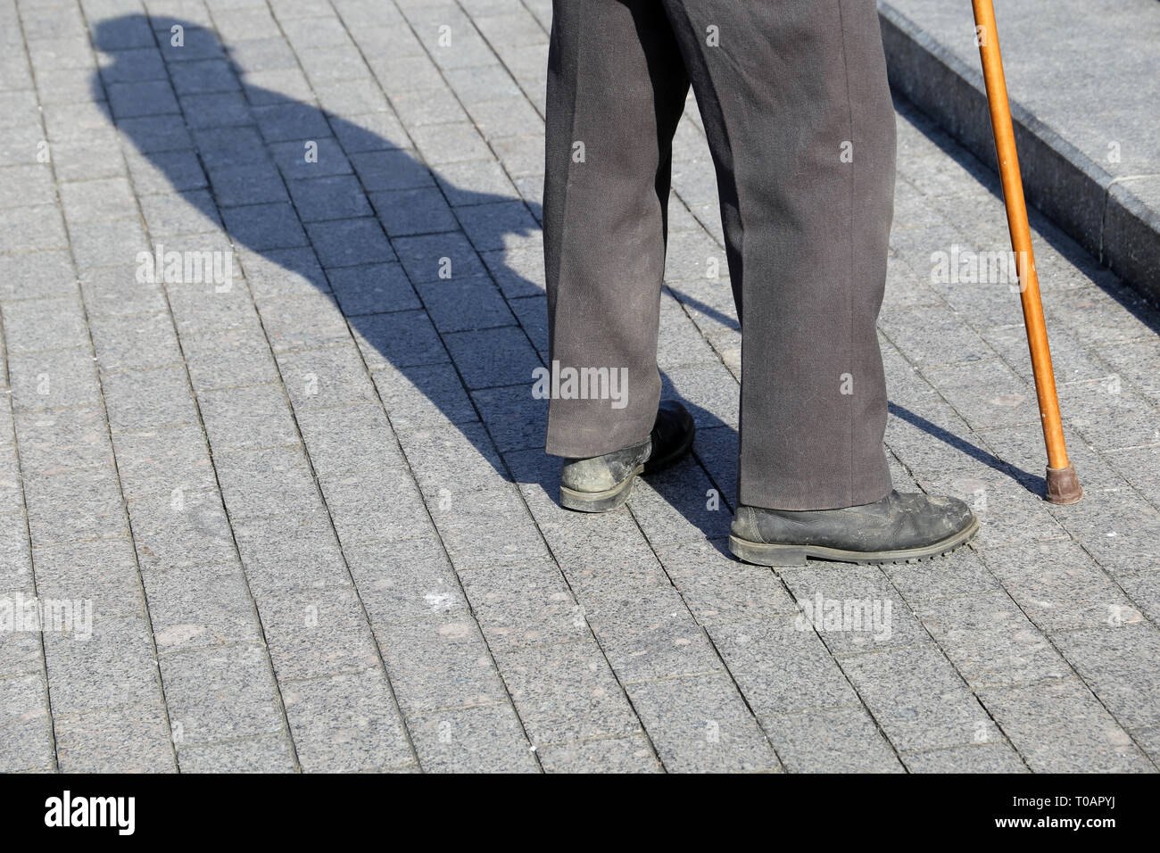 Mann mit spazierstock stehen auf der Straße in der Nähe des Schritte, Schatten auf Pflaster. Konzept der hinkt oder blind Person, Invalidität, Alter, Armut Stockfoto