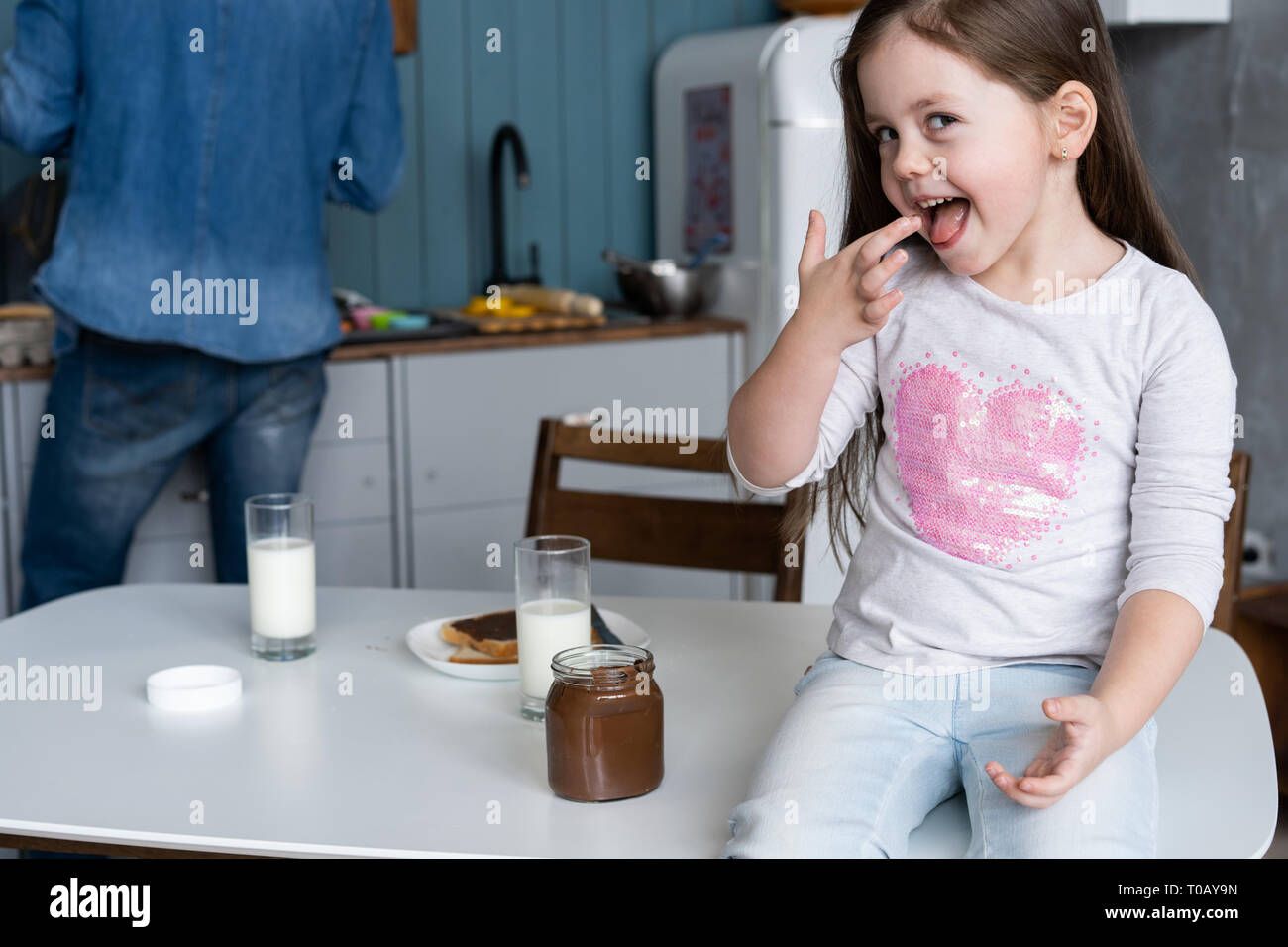 Glücklich lächelnde Mädchen essen Sandwich zum Frühstück, und wenn man die Kamera in der Küche Stockfoto