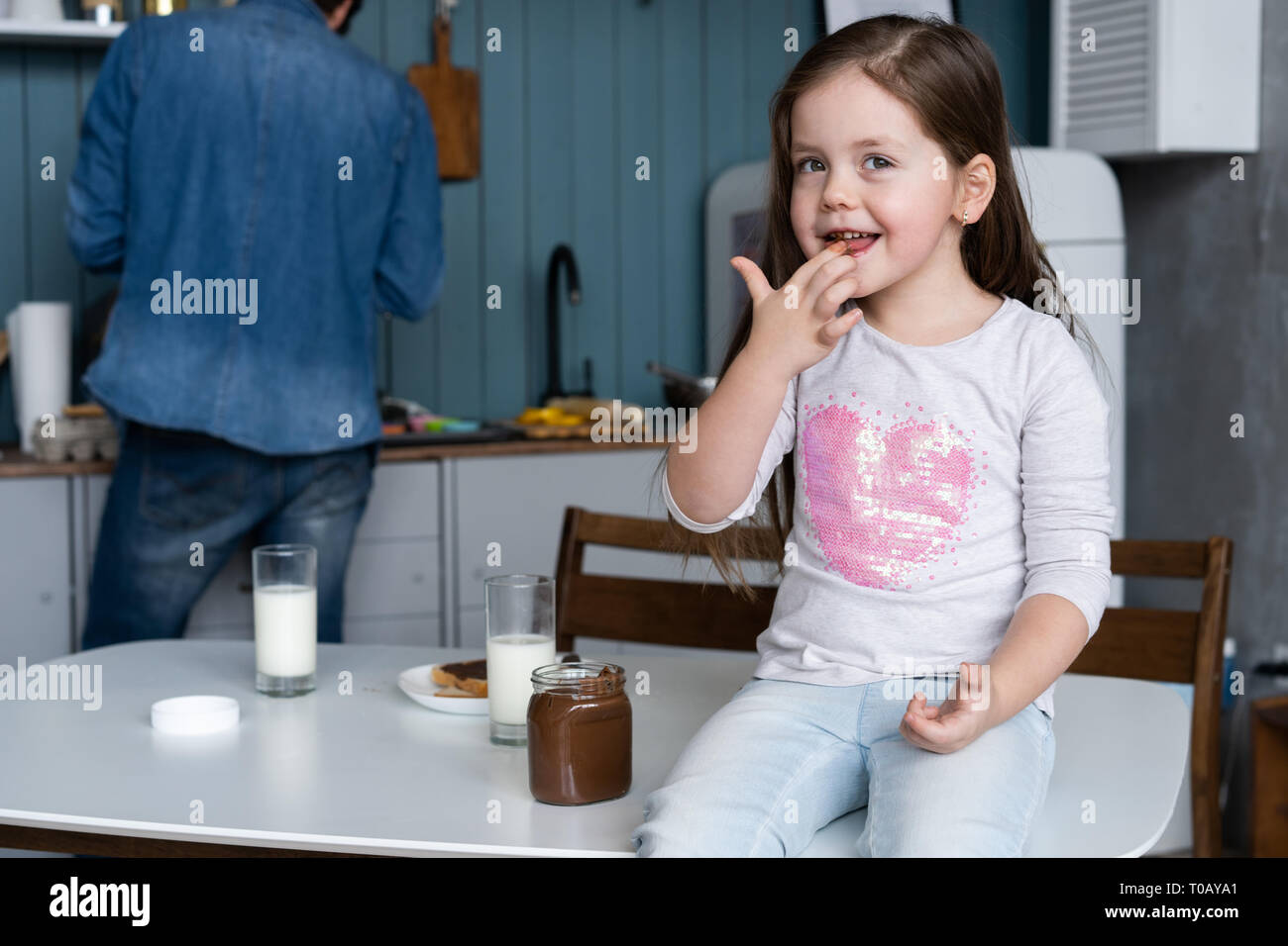Glücklich lächelnde Mädchen essen Sandwich zum Frühstück, und wenn man die Kamera in der Küche Stockfoto