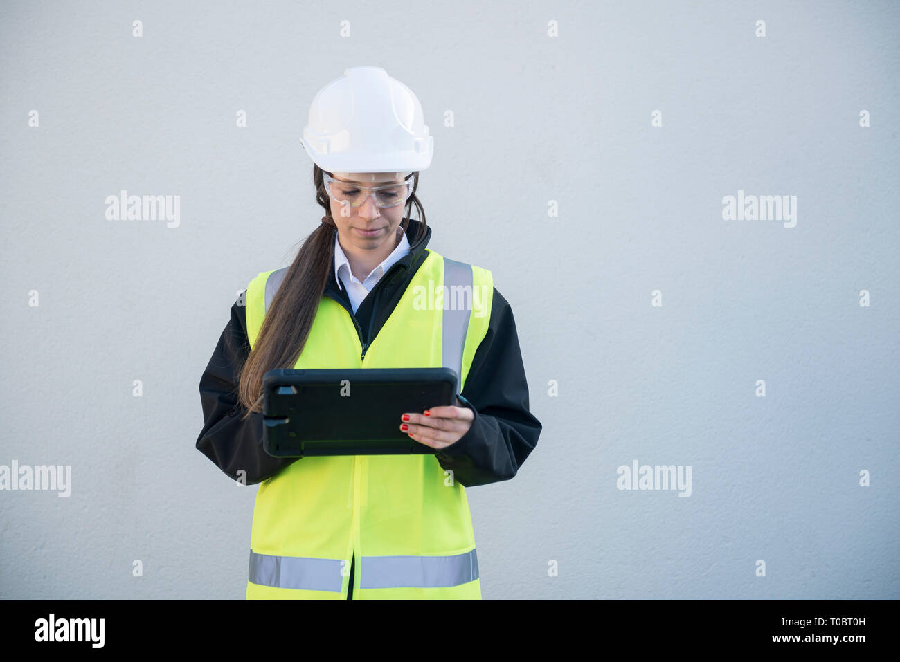 Eine weibliche Projekt Manager/Surveyor/Bauarbeiter in der High viz und Sicherheitsausrüstung verwendet ein Tablet/ipad die Eingabe von Informationen Sie angemeldet hat. Stockfoto