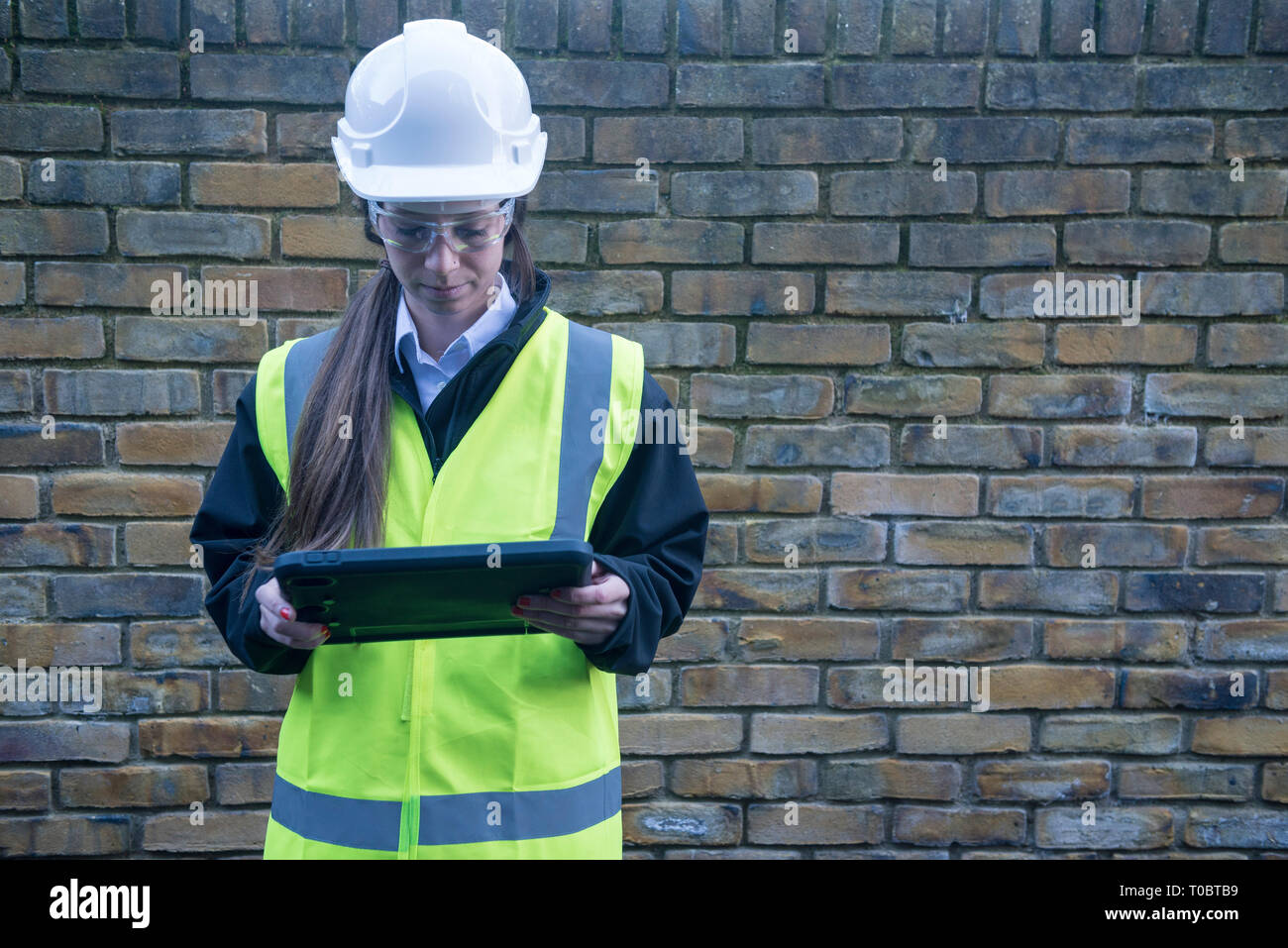Eine weibliche Projekt Manager/Surveyor/Bauarbeiter in der High viz und Sicherheitsausrüstung verwendet ein Tablet/ipad die Eingabe von Informationen Sie angemeldet hat. Stockfoto