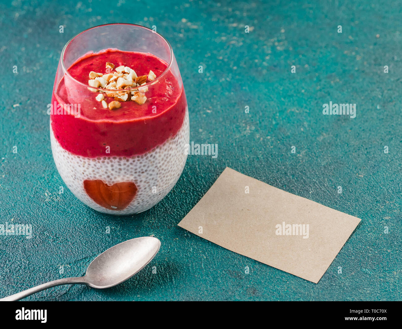 Idee für gesundes Frühstück am Valentinstag: Chia Pudding mit roten Beeren Püree, gehackte Mandeln auf und Erdbeere in der Form des Herzens. Mit leeren valentines Grußkarte für Text Stockfoto