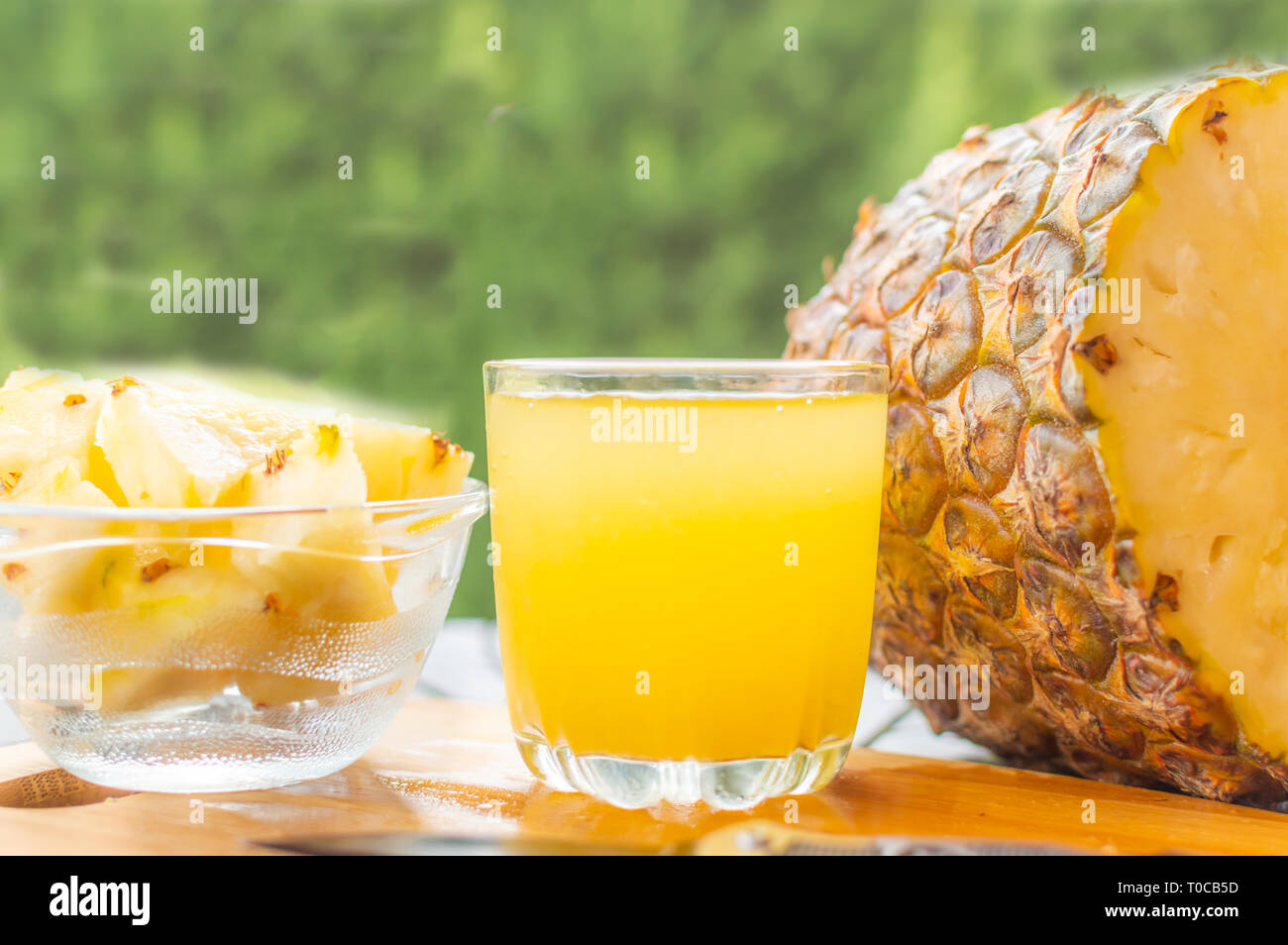 In Scheiben geschnittene Ananas gehalten auf einer hölzernen Tisch neben einem Glas mit Ananas Saft gefüllt und mit einem Glasgefäß mit Ananasscheiben Stockfoto