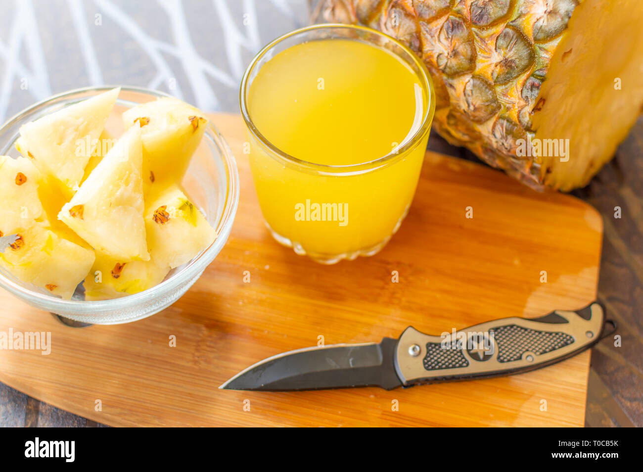 In Scheiben geschnittene Ananas gehalten auf einer hölzernen Tisch neben einem Glas mit Ananas Saft gefüllt und mit einem Glasgefäß mit ananasscheiben und ein Messer auf dem Cho Stockfoto