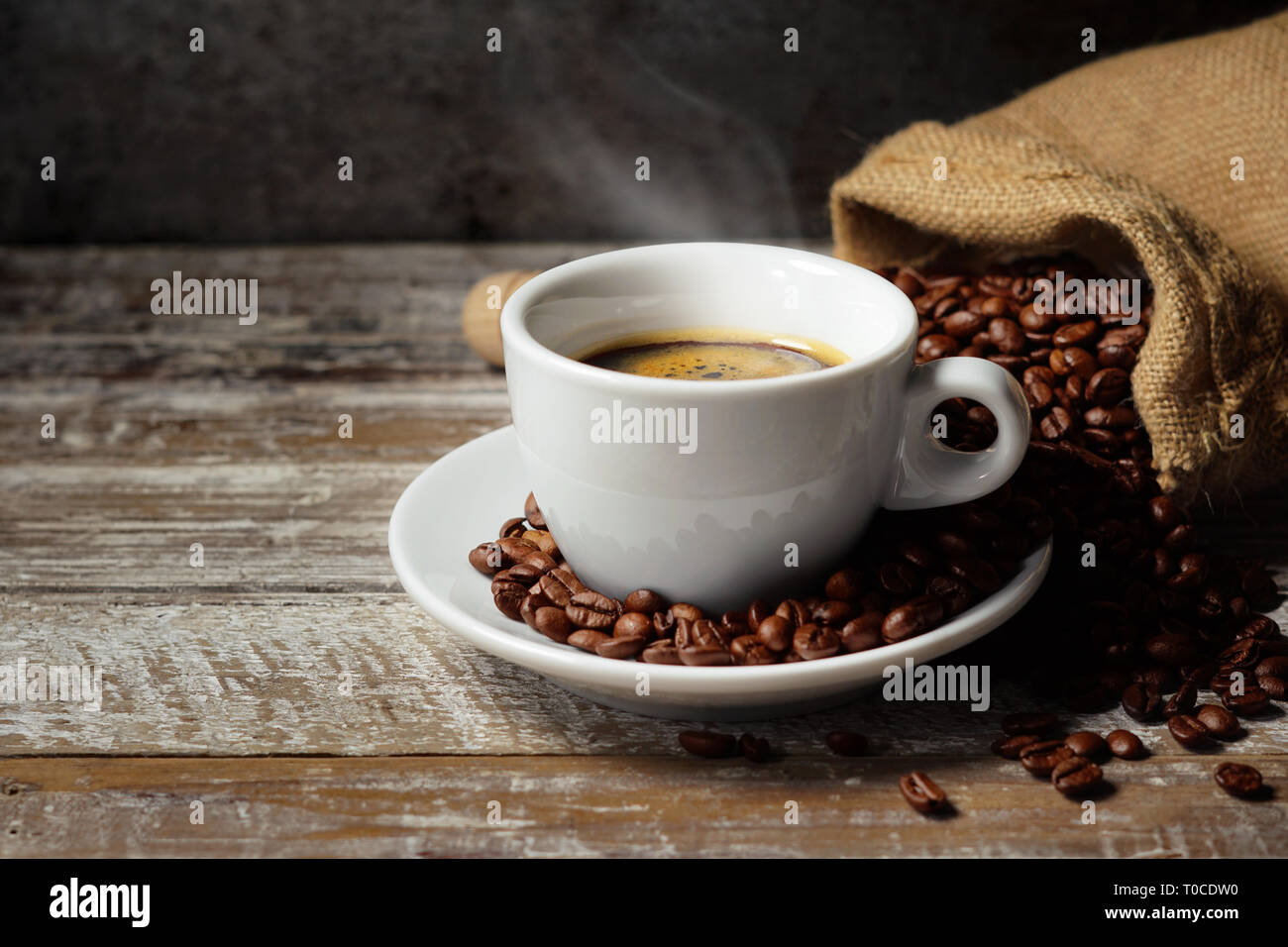 Kaffeetasse und gerösteten Kaffeebohnen in einem sackleinen Sack auf einem rustikalen Holztisch auf rostigen vintage Hintergrund. Stockfoto