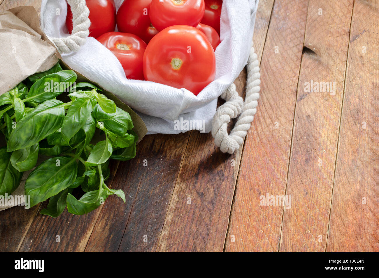 Rote Tomaten und grüne Basilikum in umweltfreundlichen Verpackungen auf Holztisch. Stockfoto