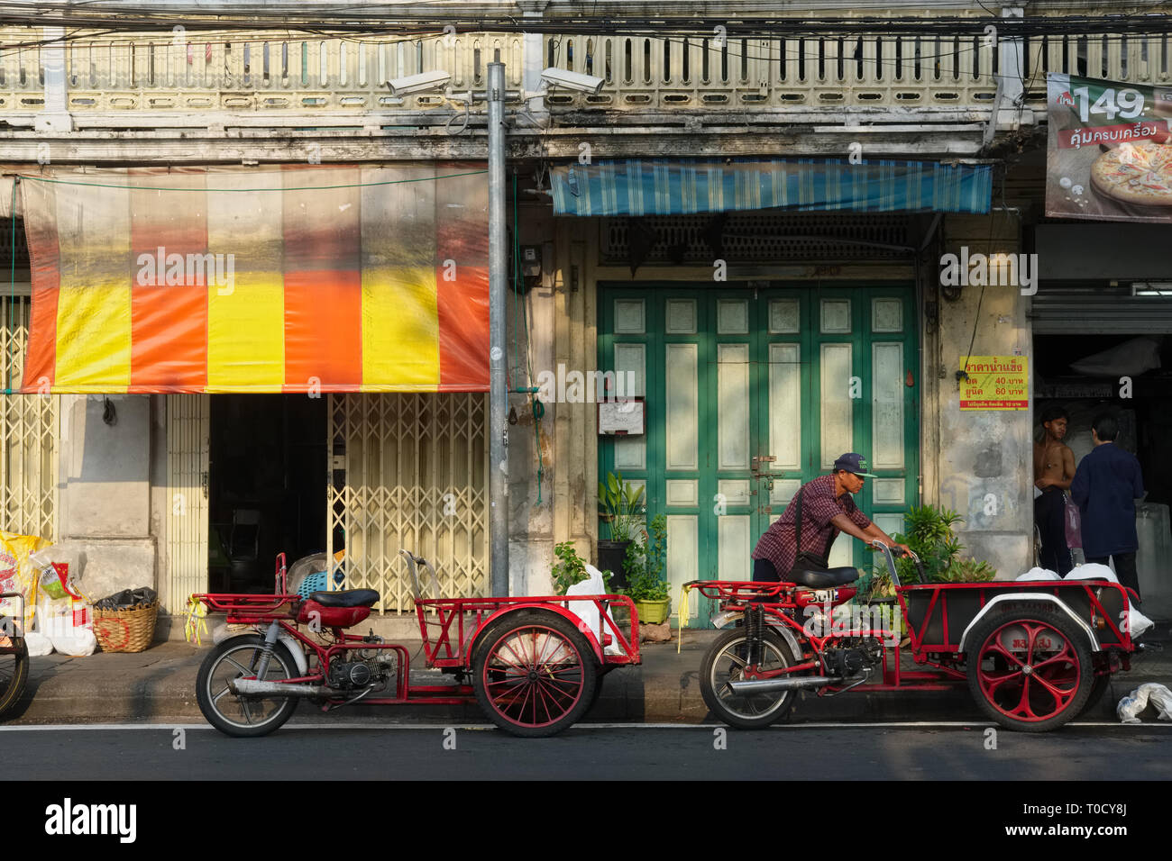 Eine Straße in der Altstadt von Bangkok, Thailand, mit Traditionellen Chinesischen Geschäftshäusern und waren auf ein Motorrad mit Last Bereich geladen werden Stockfoto