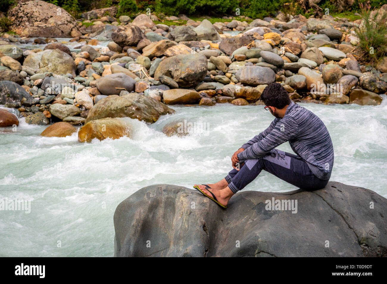 Eine Person auf einem Felsen vor einem Fluss in Pahalgam in Kaschmir sitzen Stockfoto