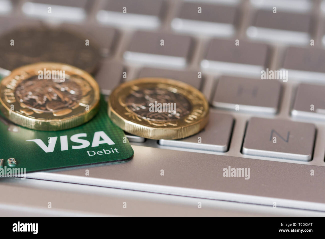 Nahaufnahme eines Visa Debit Card und Münzen auf einem Laptop Tastatur. Online Banking, Online Shopping Konzepten. Vereinigtes Königreich Stockfoto