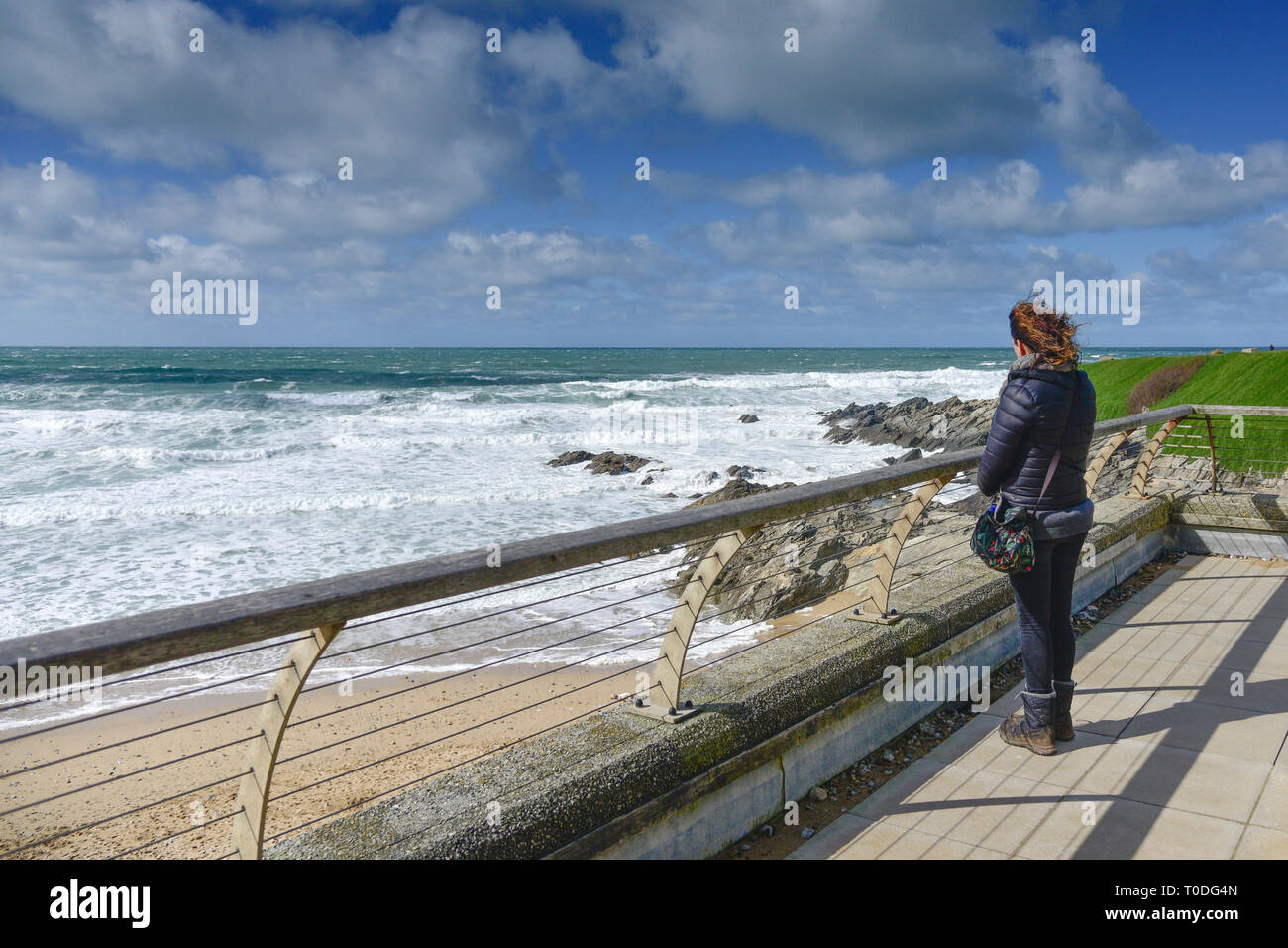 Eine Frau allein stehend an einem windigen Tag auf einem Balkon mit Blick auf den Fistral Beach in Newquay in Cornwall. Stockfoto