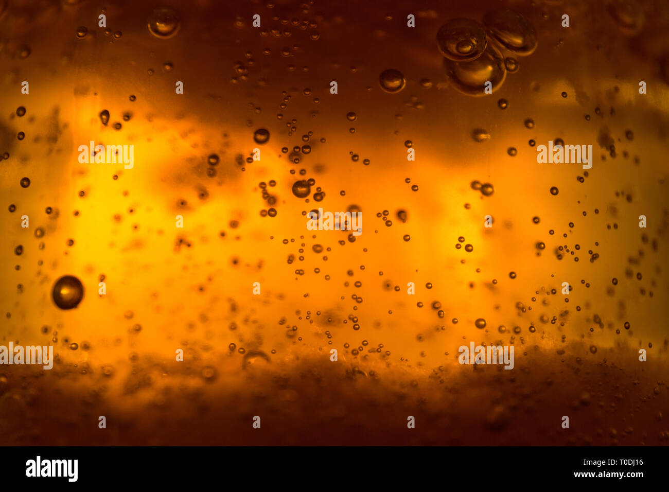 Makroaufnahme aus bernsteinfarbener Flüssigkeit mit glühenden Luftblasen und goldener Textur Stockfoto