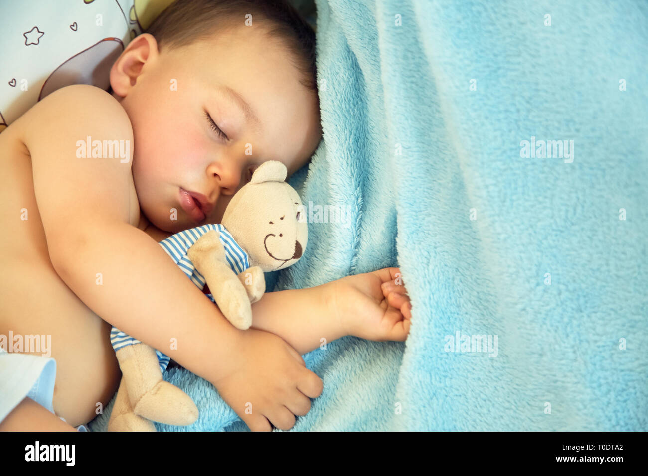 Schlafendes Baby mit einem weichen Spielzeug tragen. kleiner Junge liegt in einer Krippe auf einer blauen Decke Stockfoto