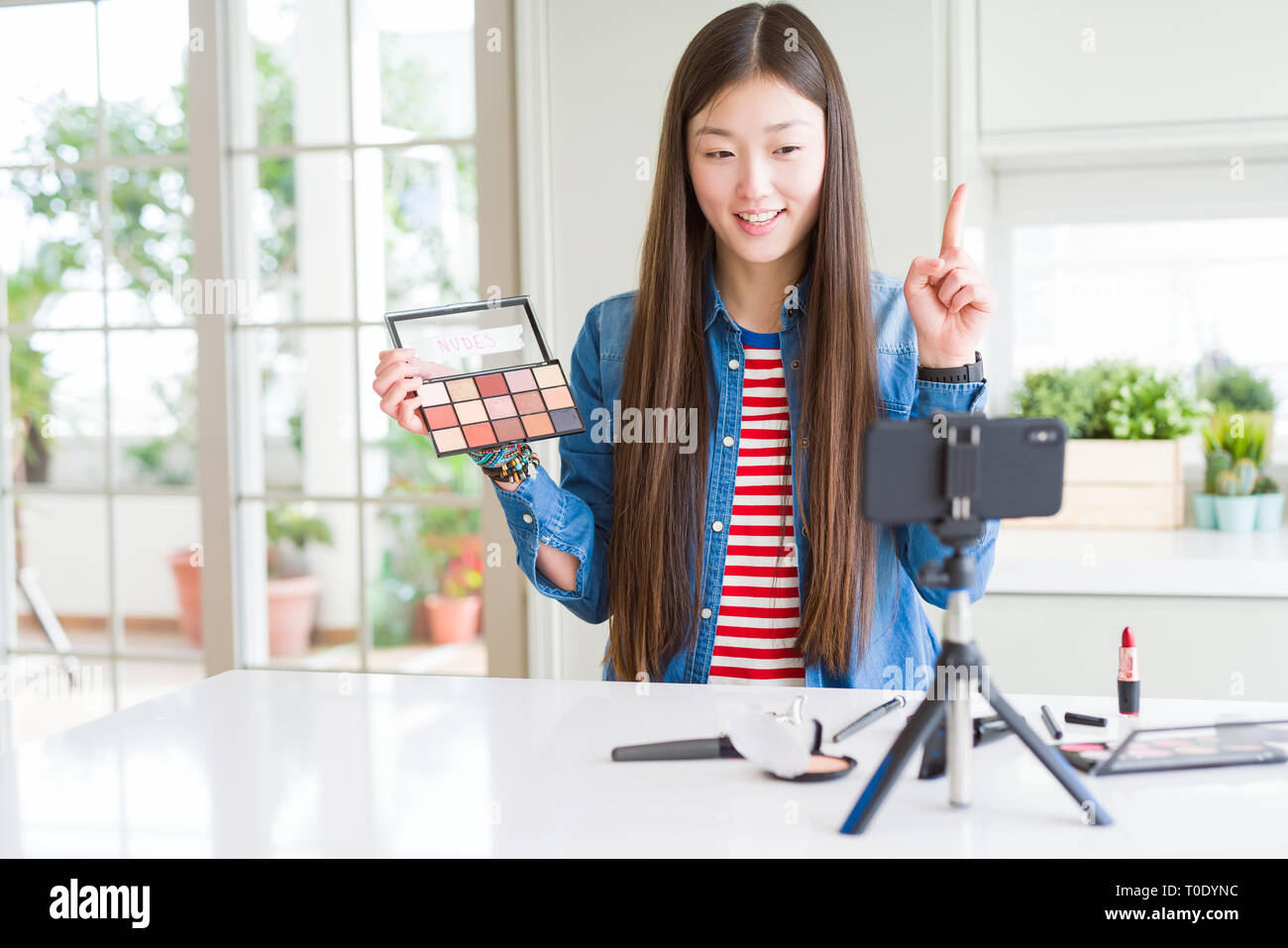 Schöne asiatische Einflussnehmer Frau Aufnahme Make-up Tutorial mit Smartphone Kamera mit einer Idee oder Frage Zeigefinger mit glücklichen Gesicht überrascht Stockfoto