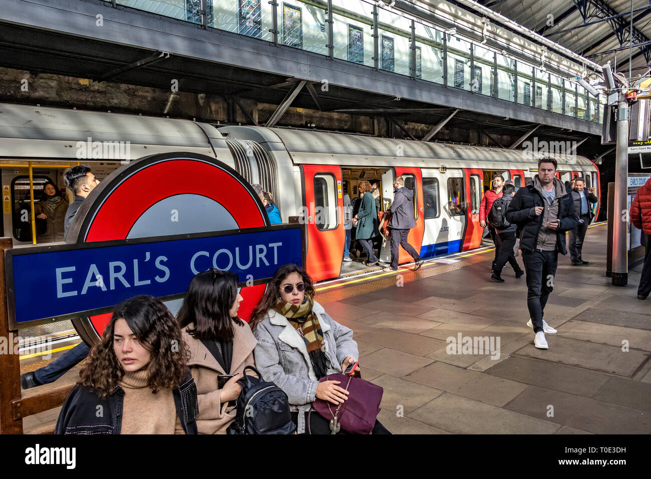 Passagiere, die auf dem Bahnsteig auf einen Zug der District Line am U-Bahnhof Earls Court in London, Großbritannien, warten Stockfoto