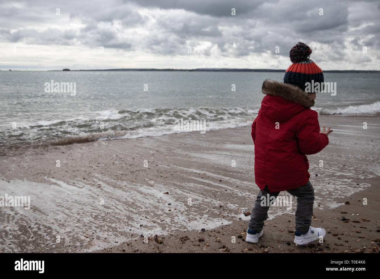 Junge zwei im roten Mantel spielen am Strand im Frühling mit Bommel hat im Alter von Stockfoto
