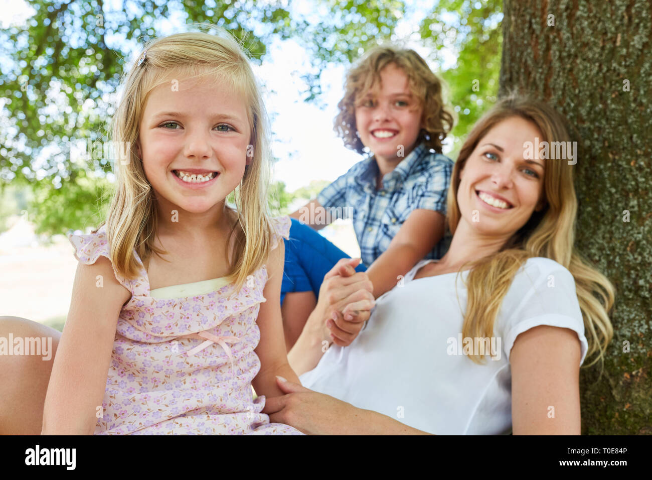 Glückliche Familie mit Mutter und zwei Kinder sitzen entspannt unter einem Stockfoto