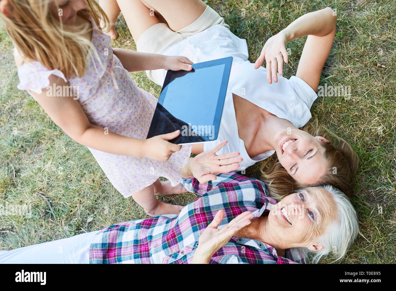 Kleines Mädchen nimmt Bild von Mutter und Oma, die mit dem Tablet Computer Stockfoto