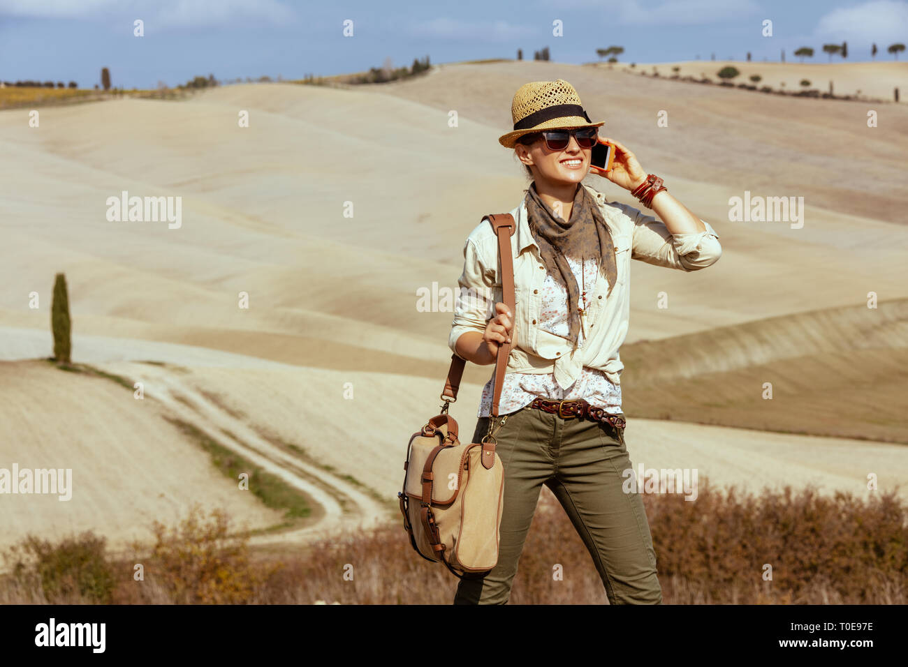 Glückliche junge Frau in Wanderkleidung mit Beutel genießen Sie im Sommer die Toskana ansehen und über ein Mobiltelefon. Stockfoto