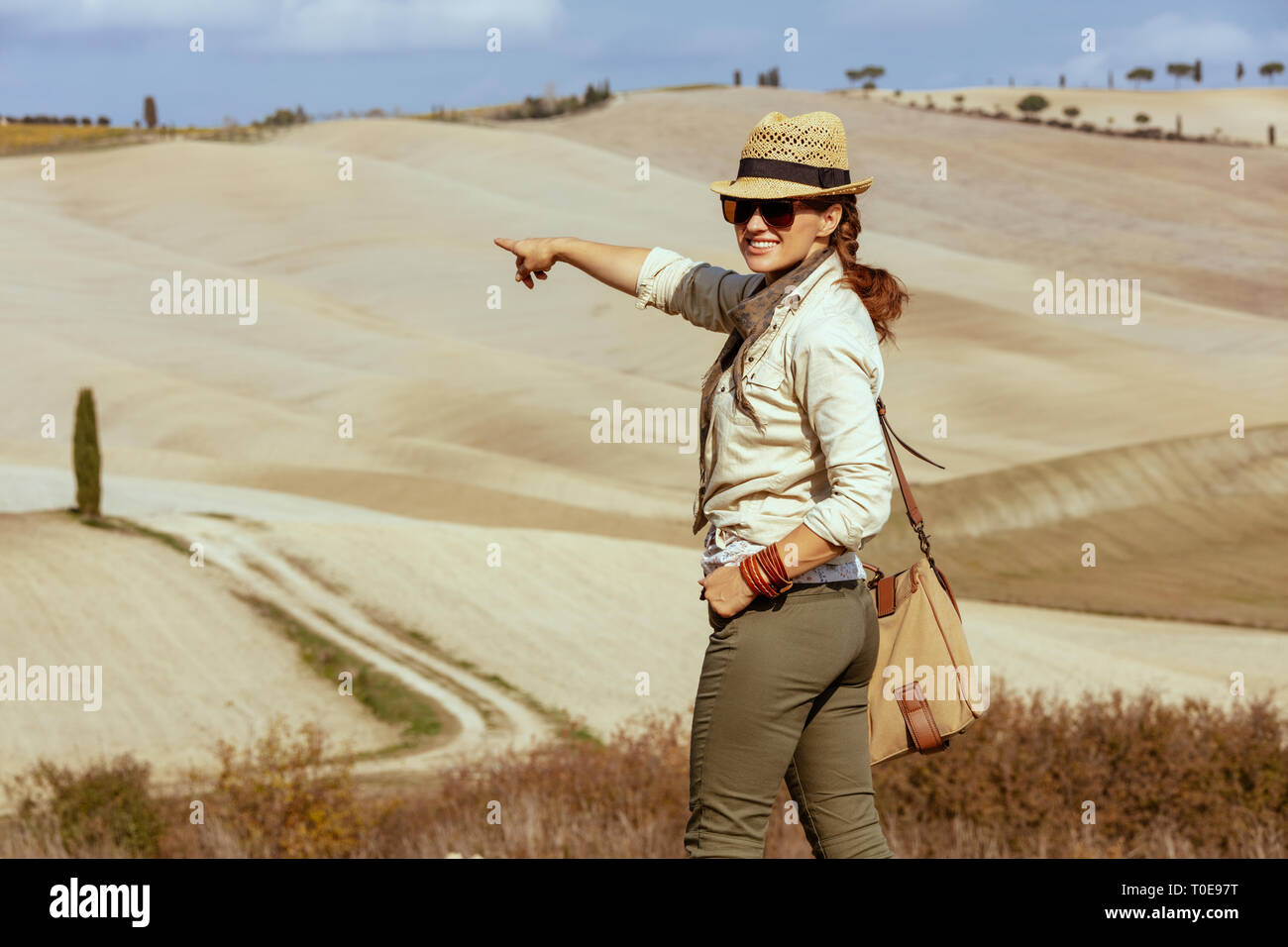 Glückliche junge touristische Frau in Wanderausrüstung mit Beutel genießen Sie im Sommer die Toskana Ansicht zeigt auf etwas. Stockfoto