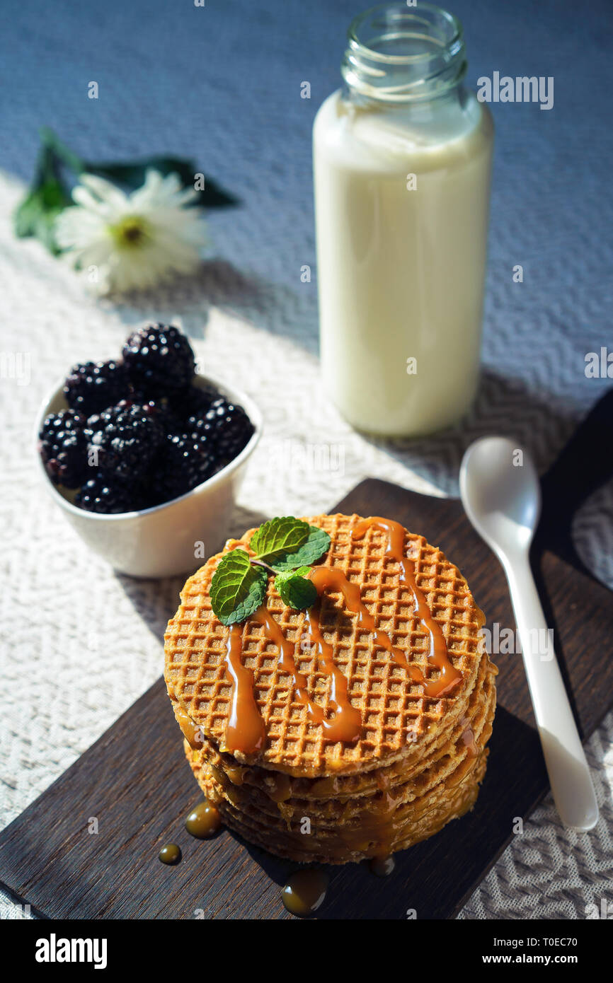 Morgen belgische Waffeln Plätzchen mit Karamellsauce und Minze auf  Holzbrett und Flasche Milch Schüssel von Brombeeren und Löffel natürliche  Farbe Tischdecke Stockfotografie - Alamy