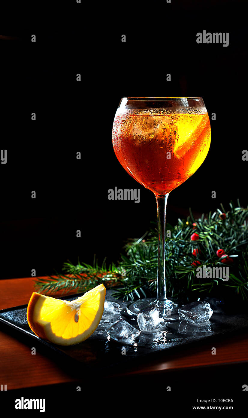Aperol Spritz Cocktail mit Orangenscheiben und Eiswürfel mit Weihnachten Tannenbaum Äste auf schwarz Fach auf dunklem Hintergrund für Feier Weihnachten Neujahr. Party Konzept Stockfoto