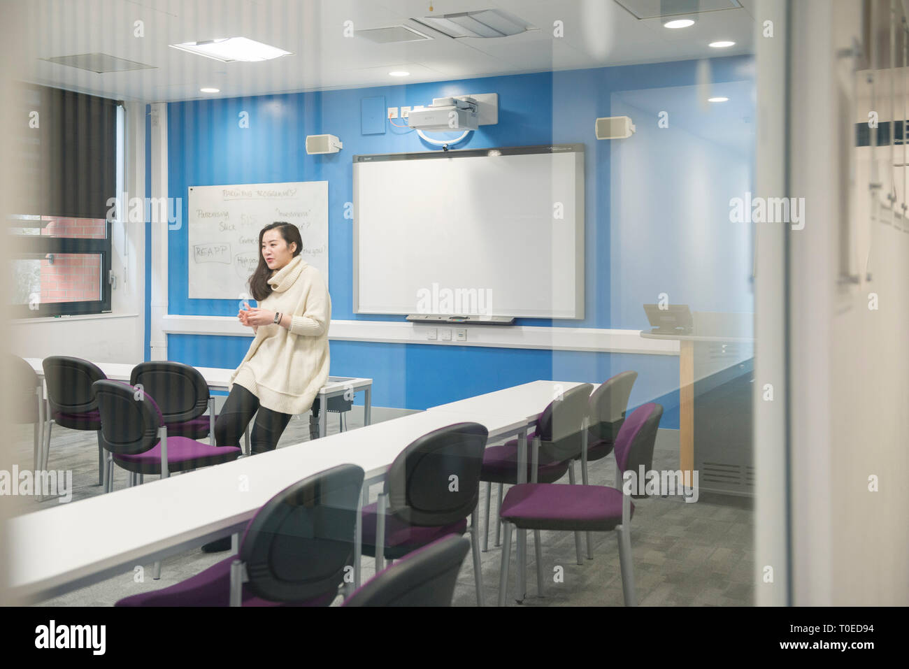 Eine Studentin sitzt auf einem Schreibtisch in einem Klassenzimmer in der Sussex University und das Gespräch mit dem Lehrer. Stockfoto