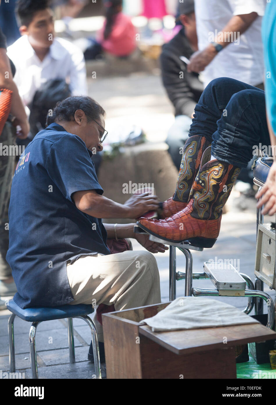 Ein Mann scheint ein Paar Stiefel mit einem Stand in der Zócalo in Oaxaca, Mexiko, 8. März 2019. Stockfoto