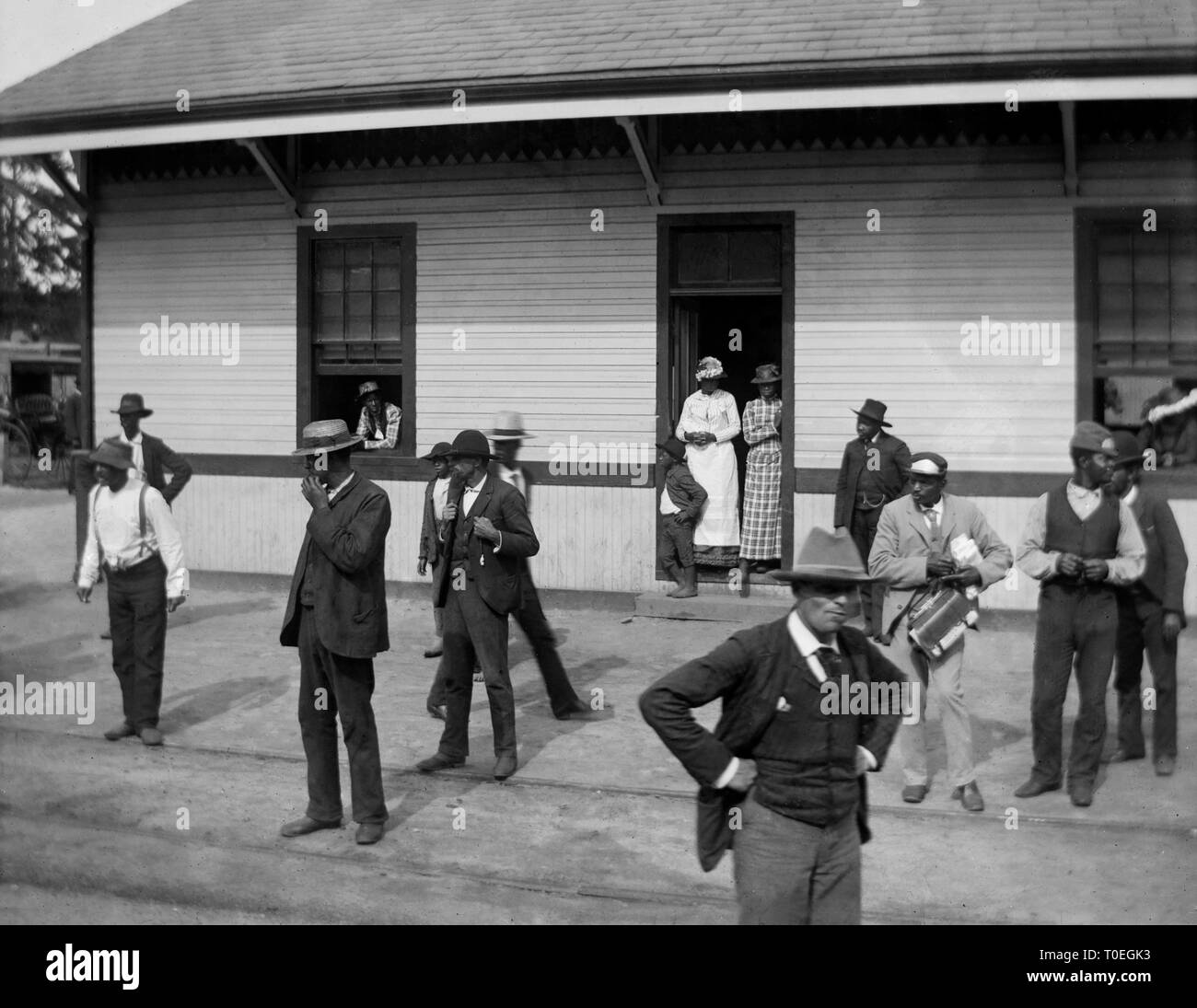 Eine Gruppe von afrikanischen amerikanischen Menschen versammeln sich auf der Plattform außerhalb eines Bahnhofs im amerikanischen Süden, Ca. 1910. Stockfoto