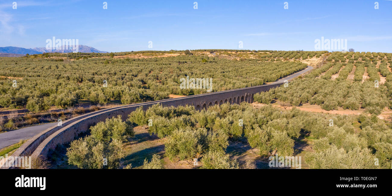 Luftaufnahme; Aquädukt mit Wasser durch Olivenhaine niedrige Einstellung Sonne Berge im Hintergrund mit blauer Himmel für copyspay Stockfoto