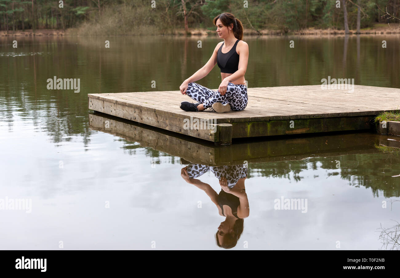 Frau sitzt auf einem Steg am See meditieren Stockfoto