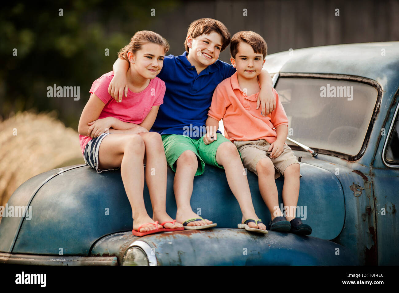 Portrait von drei jungen Geschwister zusammen sitzen auf einem alten Auto. Stockfoto