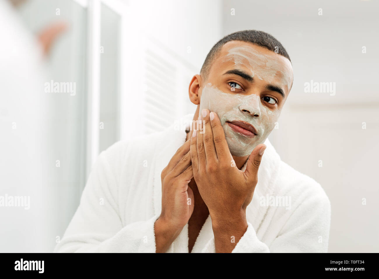 Mann im Spiegel mit weißer Tonerde Maske auf seinem Gesicht auf der Suche Stockfoto
