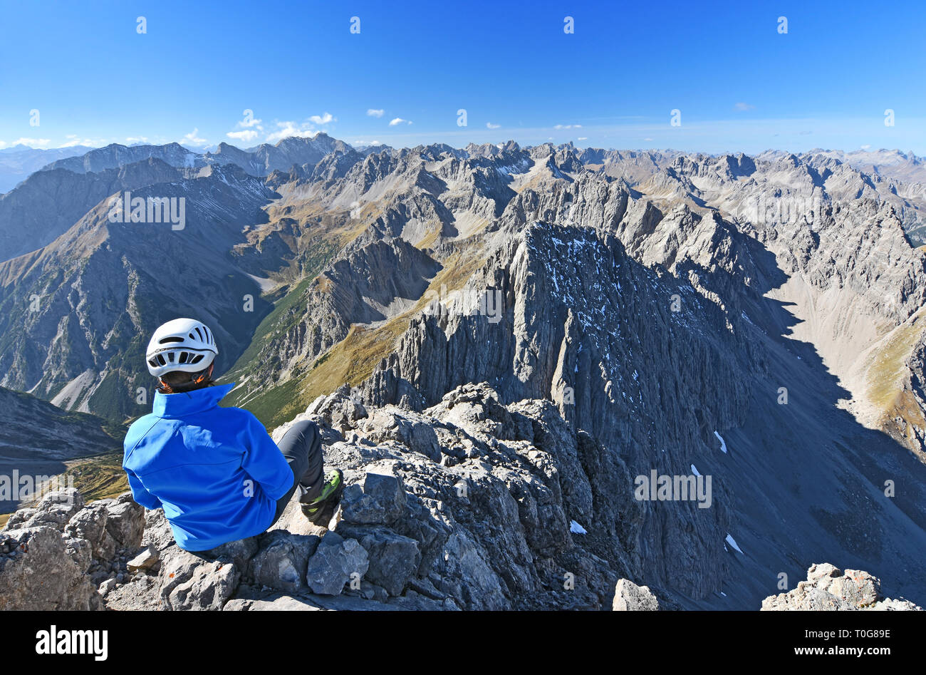 Weibliche Kletterer, die sich oben auf einem Berg sitzen (Lechtaler Alpen, Tirol, Österreich). Alpine Landschaft mit felsigen mounrains und blauer Himmel. Stockfoto