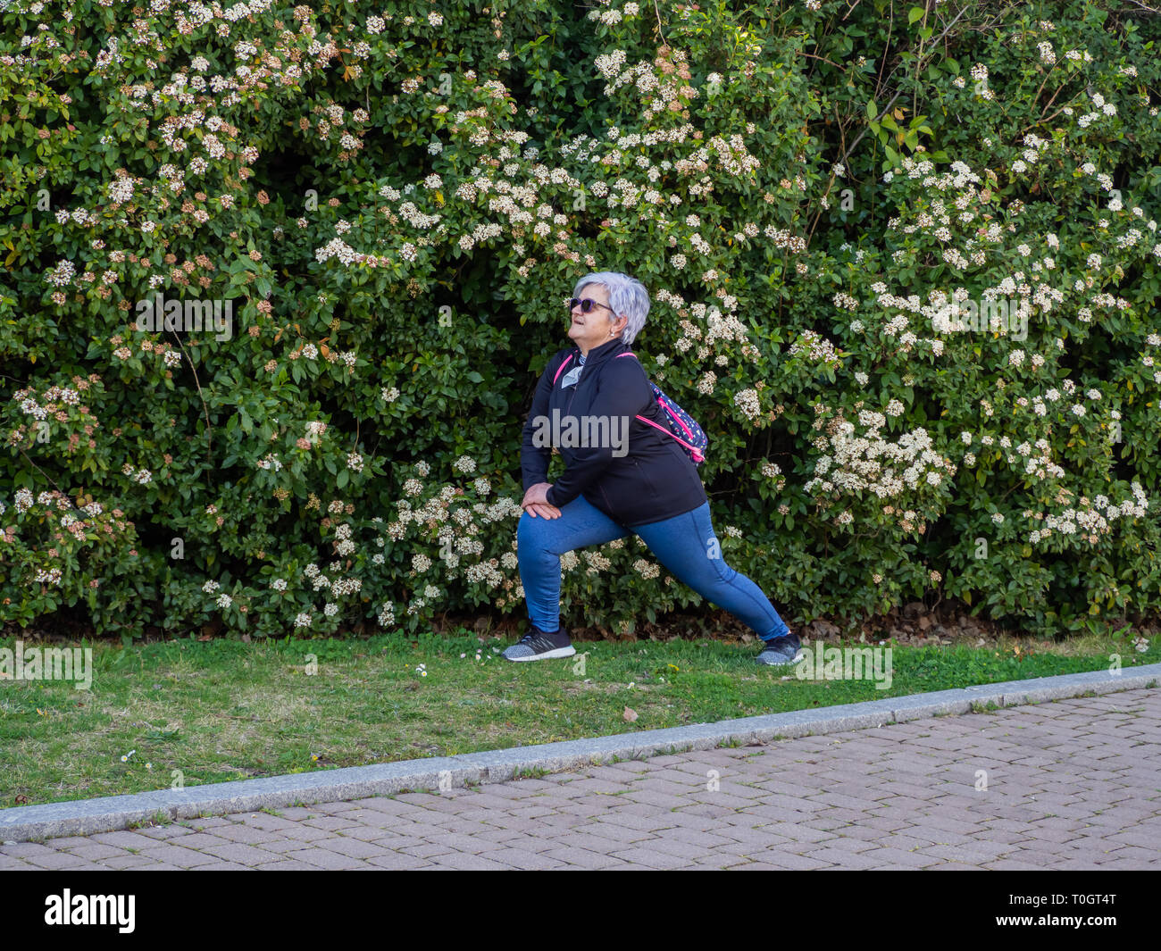 Eine ältere Frau mit weißen Haaren üben Gymnastik in einem städtischen Park Stockfoto