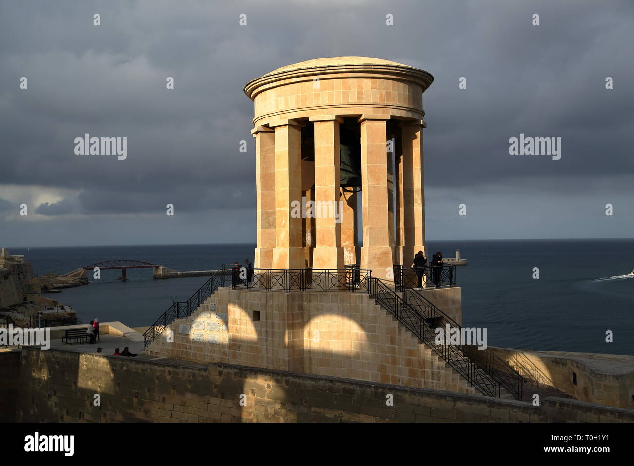 Belagerung Bell War Memorial in schönen sunste Licht, Valetta, Malta, Meer, die Mauer der Festung, Brücke über das Meer, wirbelnde Wolken im Himmel. Stockfoto
