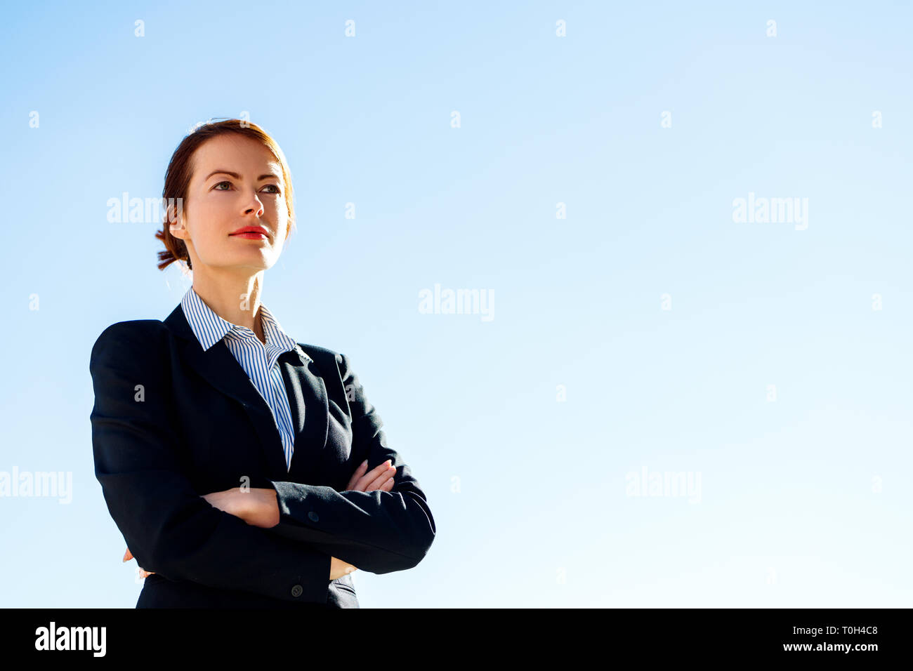 Business Frau mit gekreuzten Händen steht gegen den klaren blauen Himmel. Stockfoto