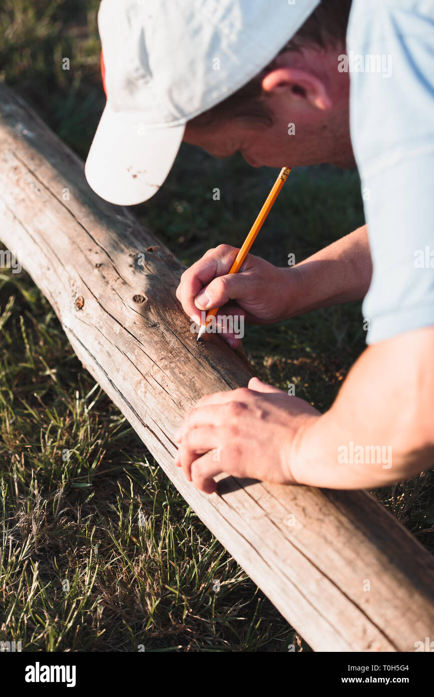 Mann, Mark mit Bleistift nach dem Messen von Holz im Garten arbeiten Stockfoto