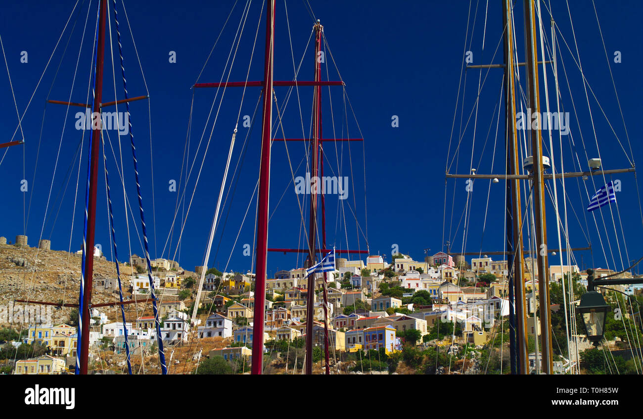 Simi Insel mit mehreren Häusern und Masten von Segelboote im Hafen gefärbt. Stockfoto