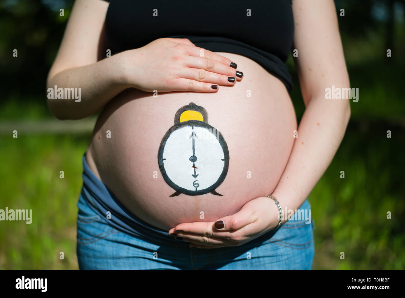 Schwangere Frau mit Uhr auf Ihrem bemalte Bauch Stockfoto